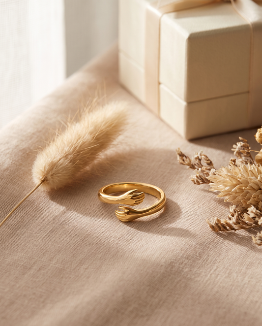 Bague Câlin ajustable dorée, deux mains enlacées, posée sur lin beige